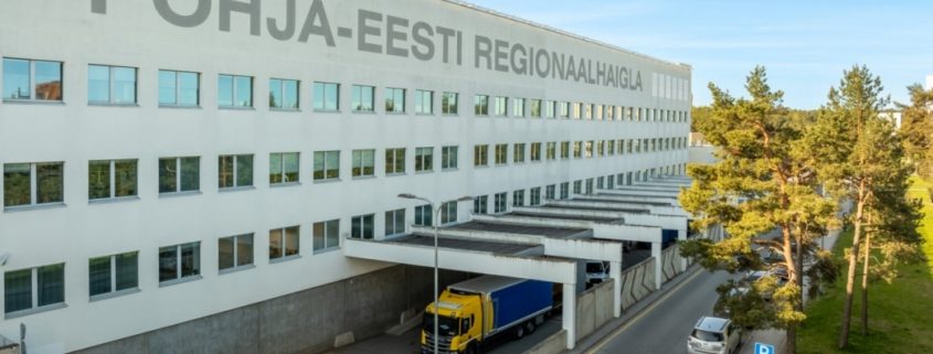 Suur valge hoone, mille fassaadile on kirjutatud PĂHJA-EESTI REGIONAALHAIGLA, millel on mitu akent, kollane ja sinine veoauto ning puudega vooderdatud sĂ”idutee-paik kukkumise ennetamine foorum 22. septembril.