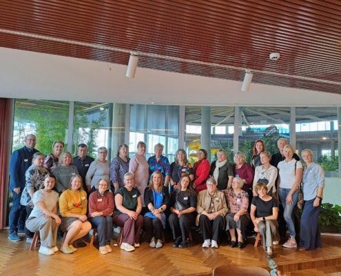 Omastehooldajate tugigrupi juhtide avaseminaril osalejad ühispildil kahes reas klaasseina ees, mille taga paistavad veekeskuse liumäed ja rohelised taimed.